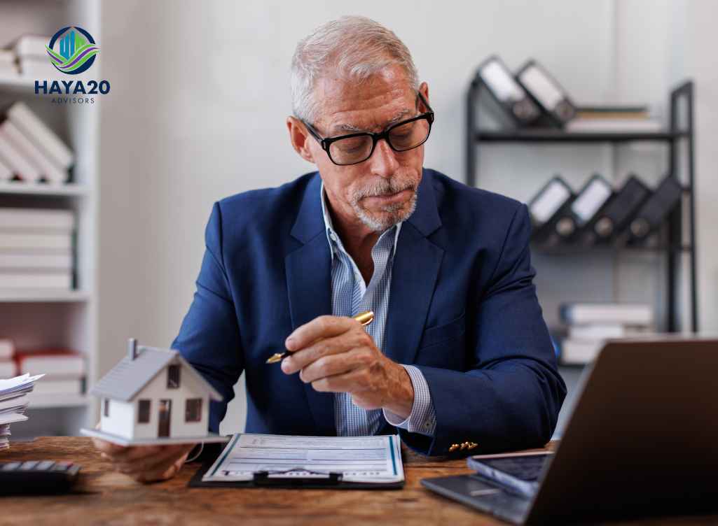 Senior financial advisor reviewing paperwork beside a house model.